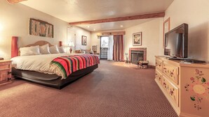 A spacious bedroom with a large bed, a television, a fireplace, and a balcony with curtains. - El Pueblo Lodge (Taos)