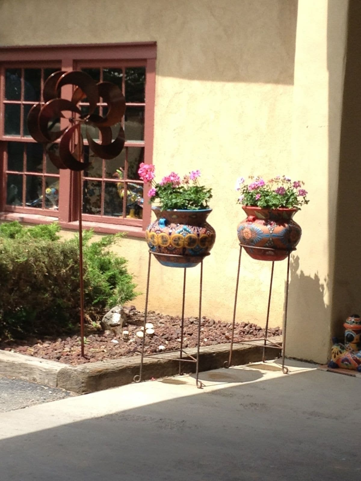 Two potted plants on metal stands in front of a building with a window.