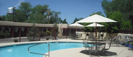 A swimming pool with lounge chairs and umbrellas, surrounded by a fence and trees.