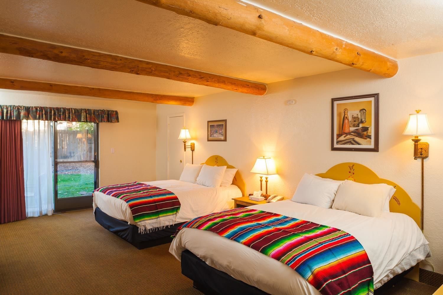 A hotel room with two beds, a large window with curtains, and a wooden ceiling beam.