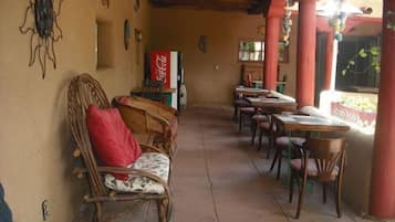 A covered outdoor seating area with wicker furniture, a Coca-Cola refrigerator, and a view of a garden.