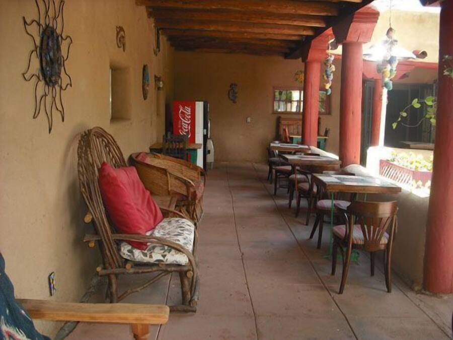 A covered outdoor seating area with wicker furniture, a Coca-Cola refrigerator, and a view of a garden.