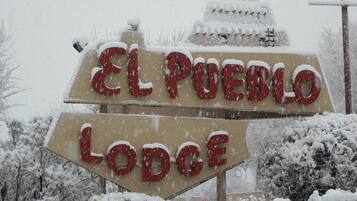 A sign for 'El Pueblo Lodge' with snow accumulation.