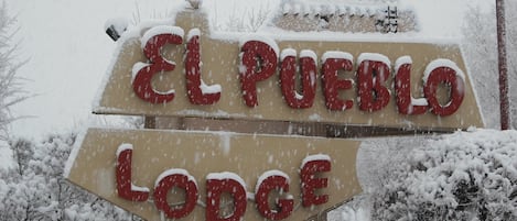 A sign for 'El Pueblo Lodge' with snow accumulation.