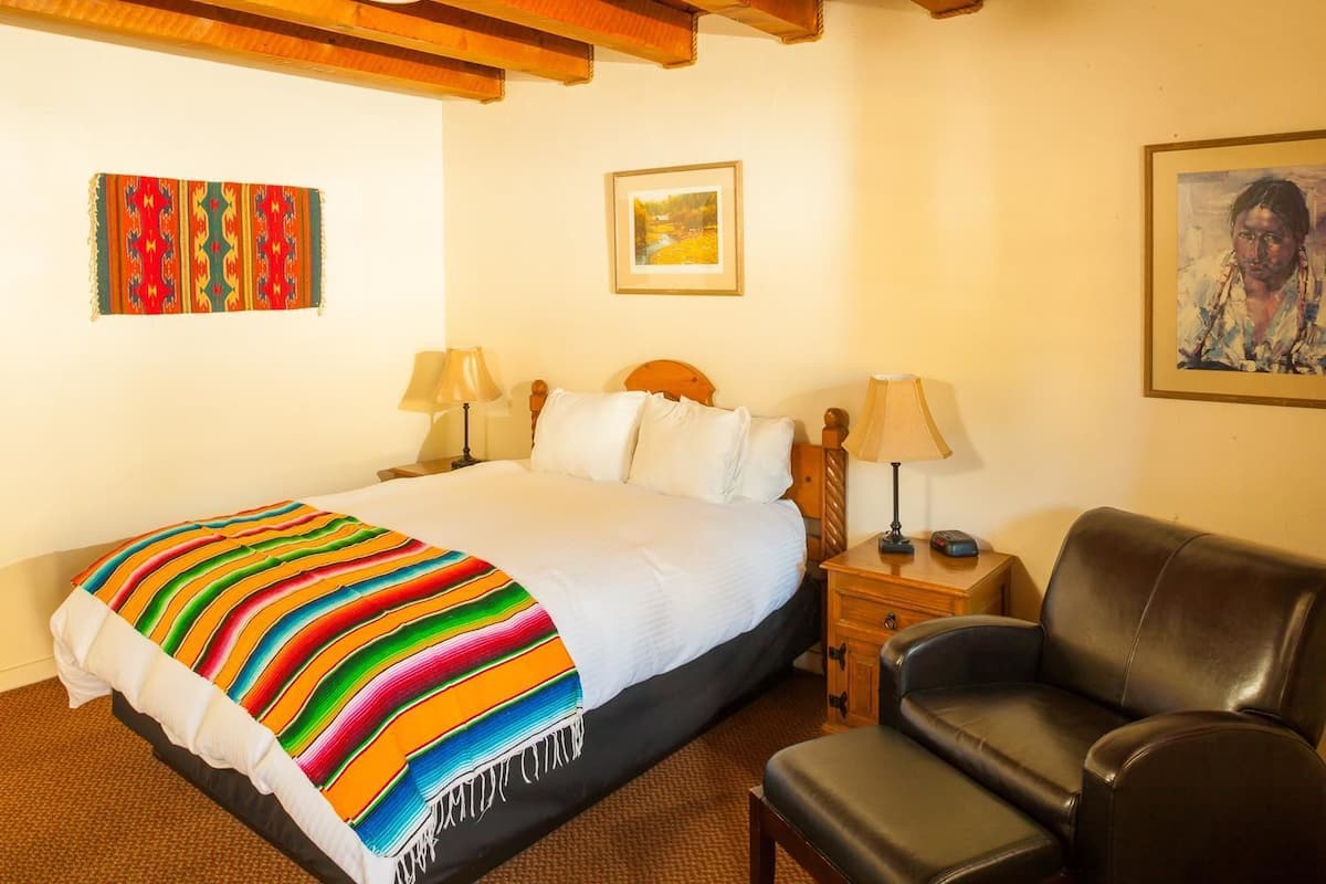 A hotel room with a large bed, two bedside tables, a black leather chair, and a framed picture on the wall.