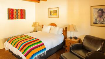 Habitación de hotel con una cama grande, dos mesitas de noche, un sillón de cuero negro y un cuadro en la pared.