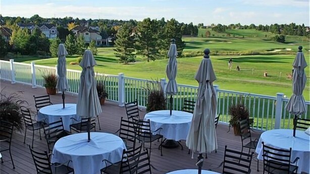 Eine Terrasse mit runden Tischen und Stühlen mit Blick auf einen Golfplatz.