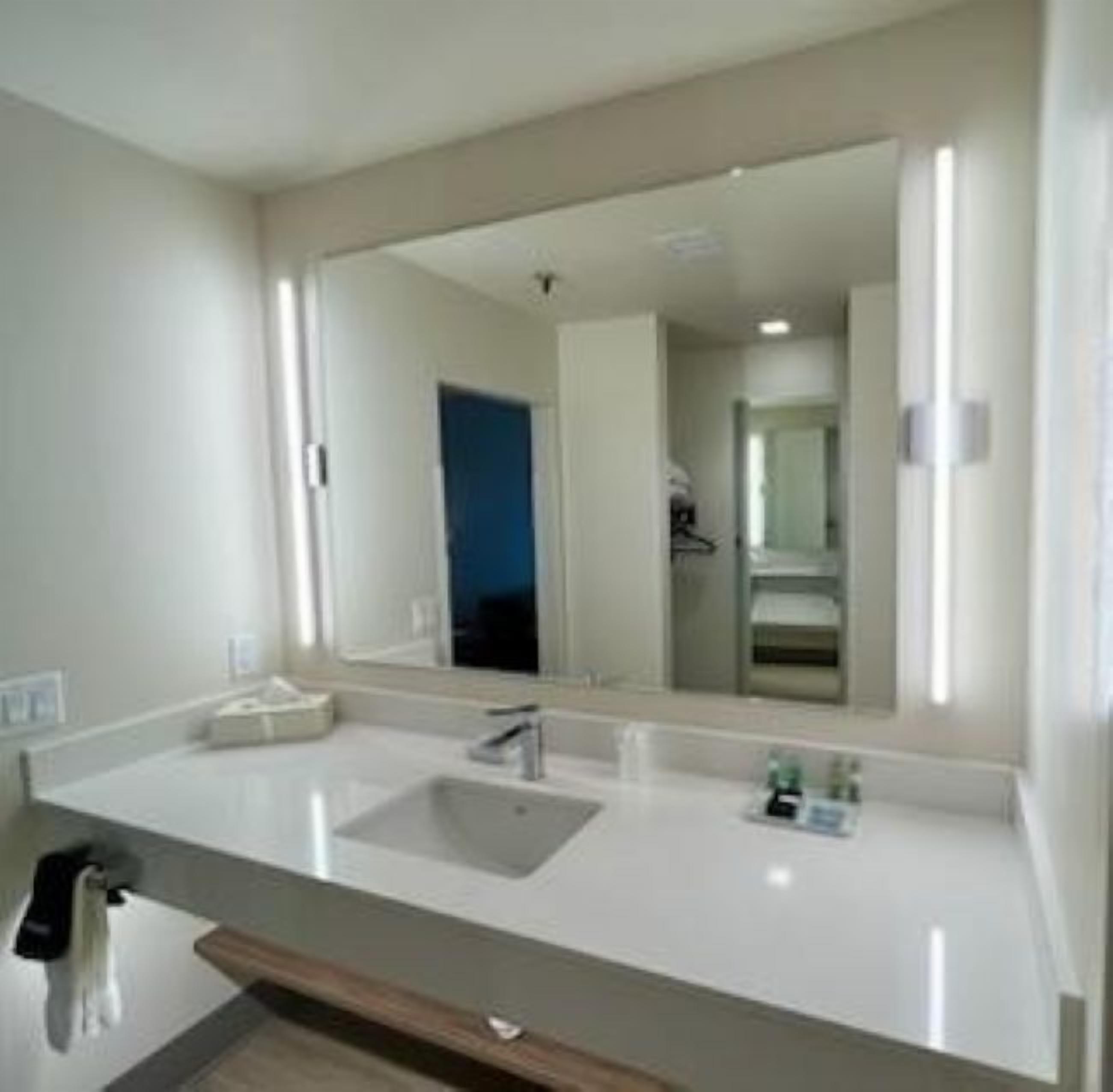 Un baño moderno con un espejo grande, un lavamanos y una zona de ducha.