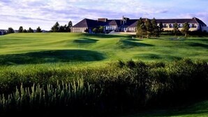 Ein Golfplatz mit Clubhaus und Bäumen im Hintergrund.