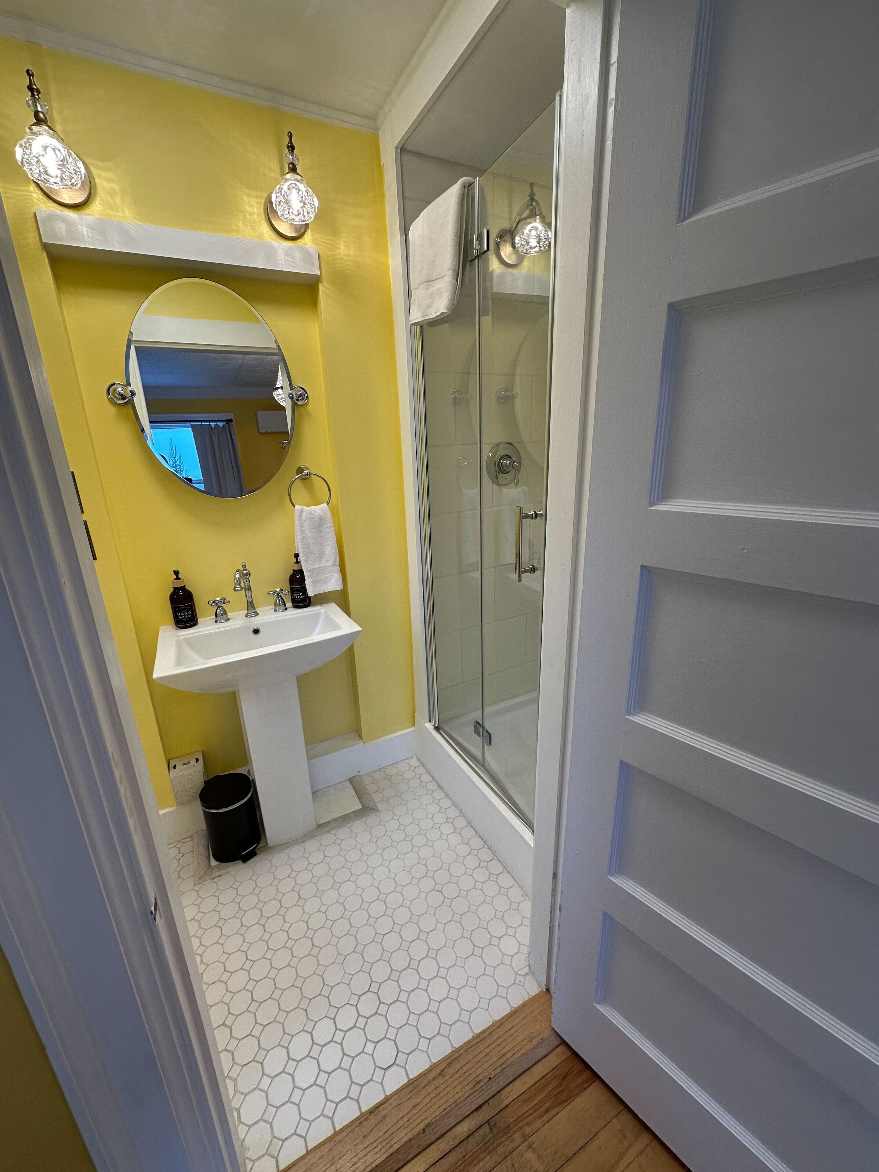 A bathroom with a yellow wall, a white sink, a mirror, and a glass shower enclosure.
