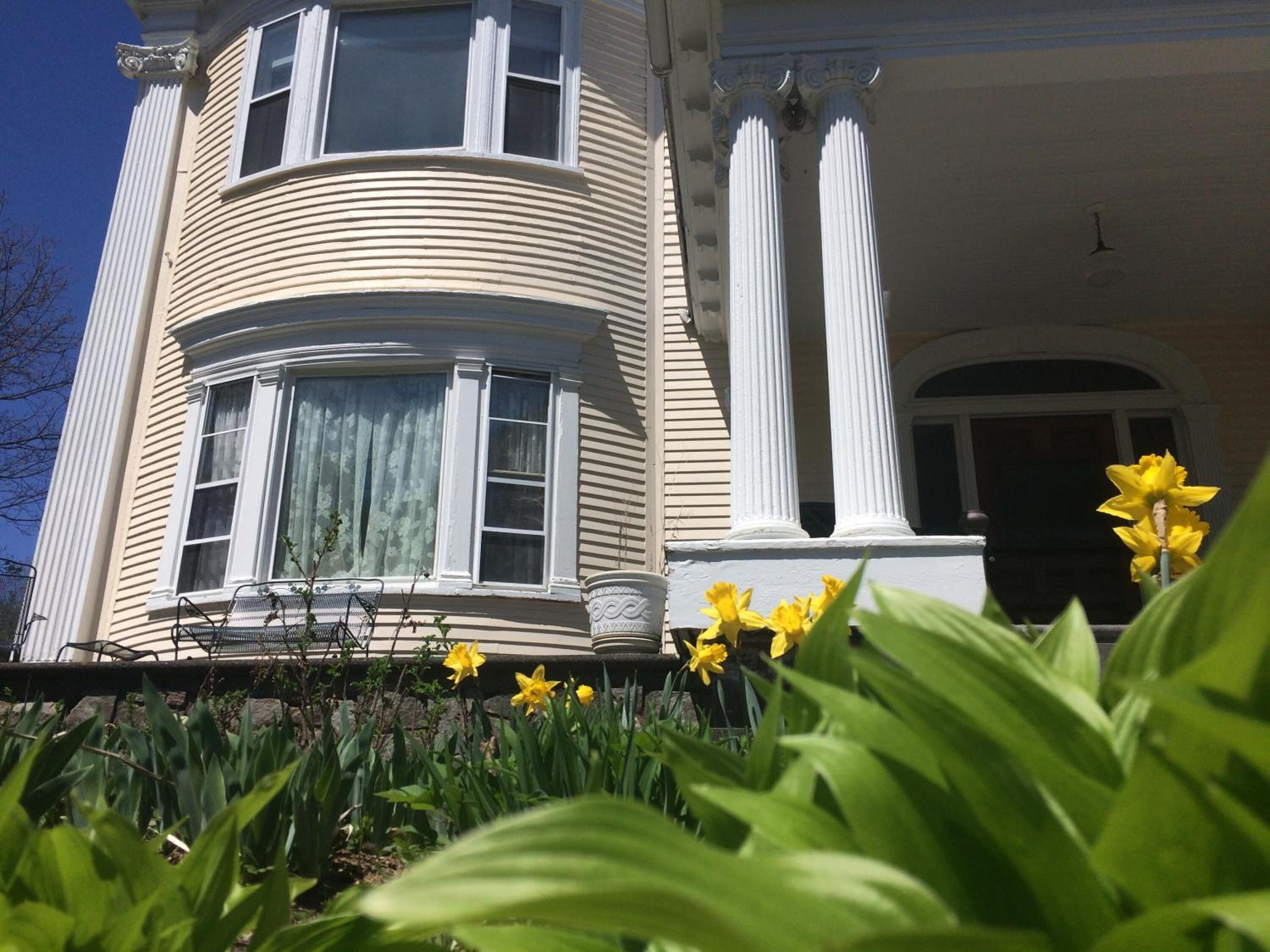 A two-story house with a curved facade, large windows, and a front porch with a bench.