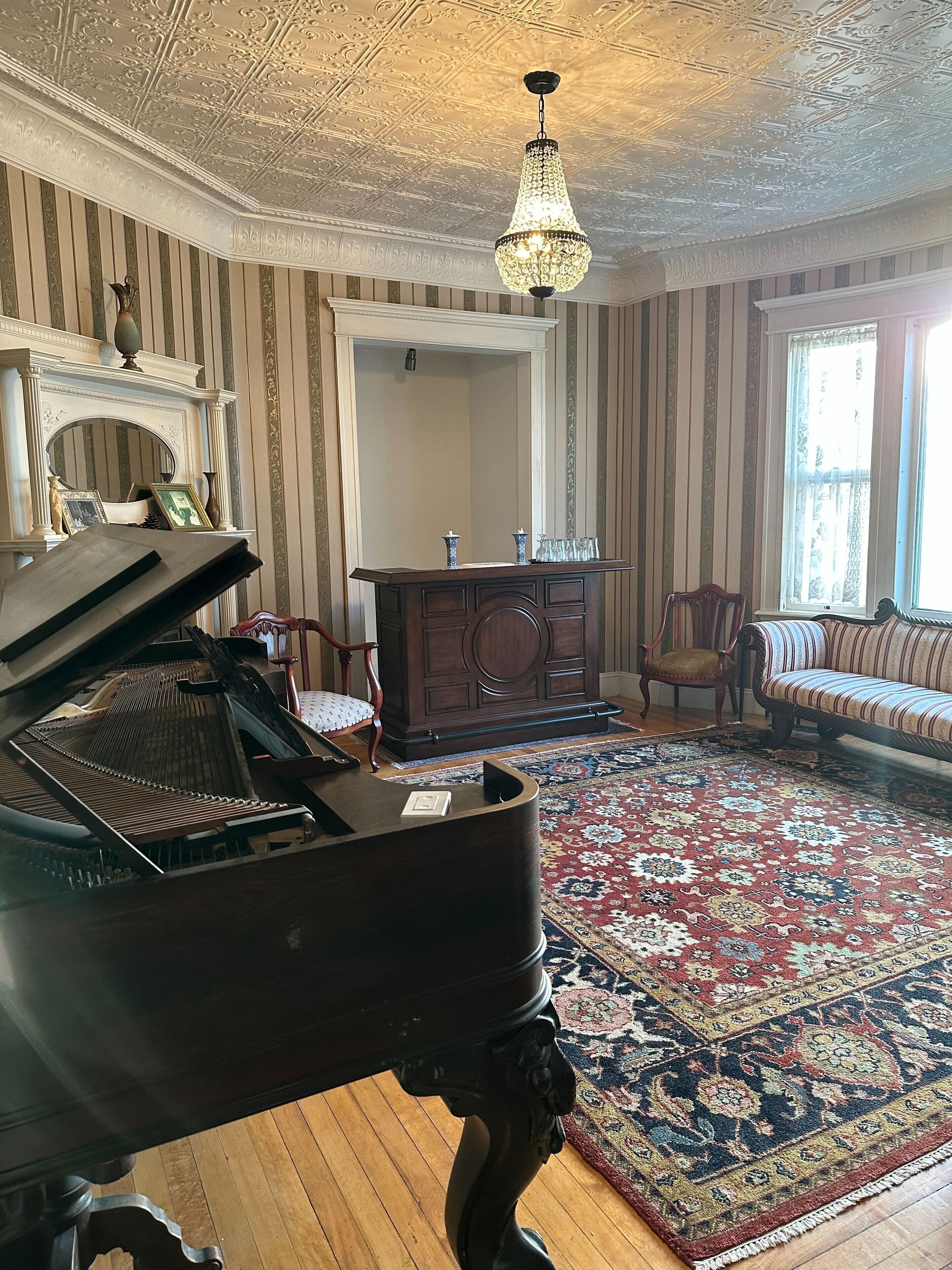 Une vaste pièce agrémentée d’un magnifique piano à queue, d’une cheminée, d’un grand miroir et d’un tapis à motifs.