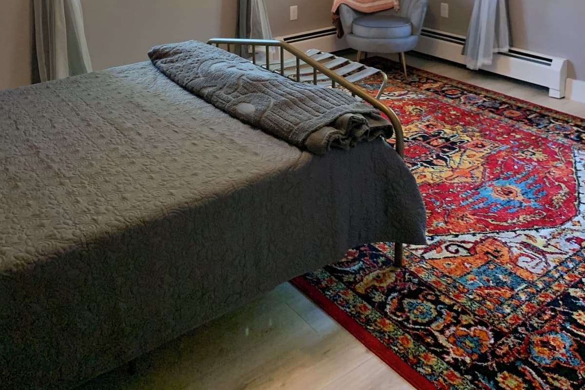 Un dormitorio con cama, una silla, un tapete y una araña.