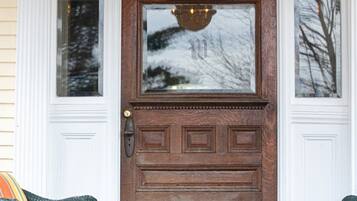 A wooden front door with a glass panel, flanked by white doors, and two wicker chairs with cushions in front.