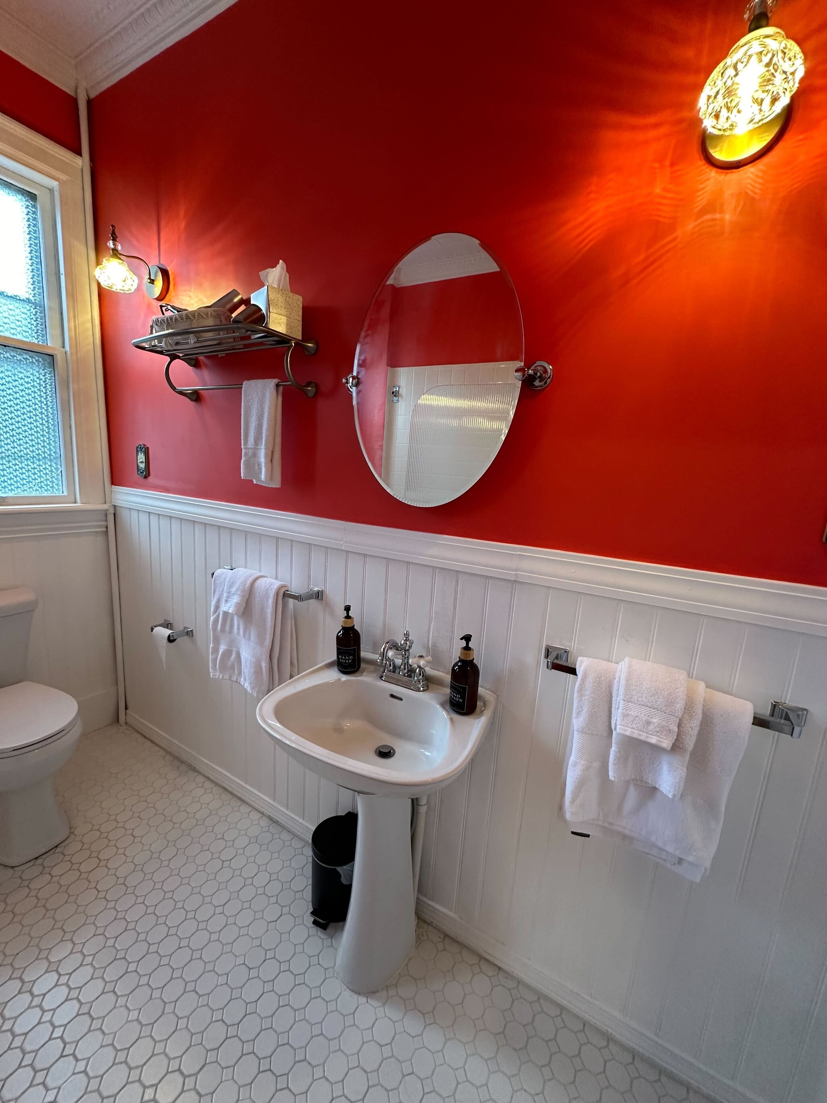 A bathroom with a red wall, white vanity, and a white toilet.