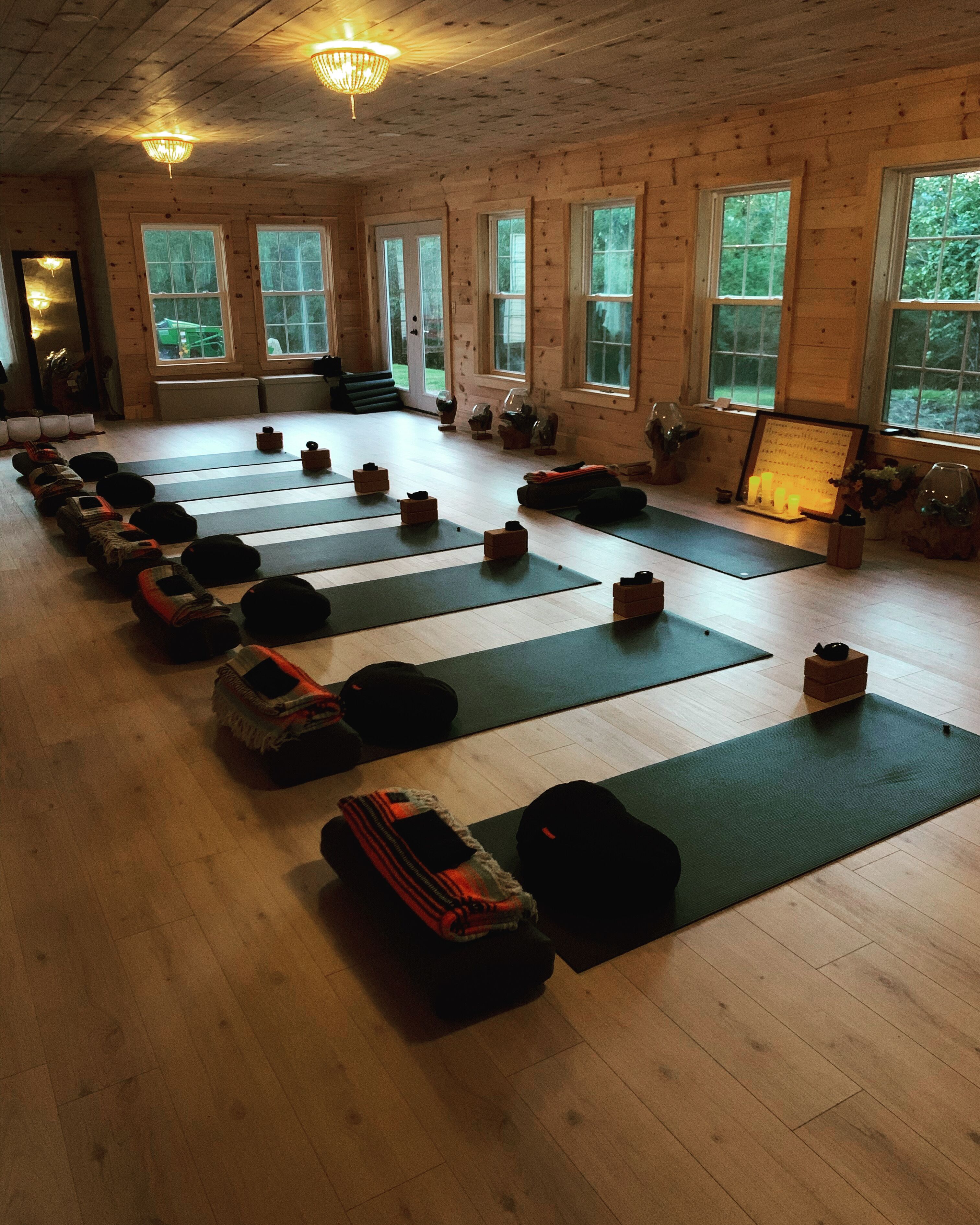 Ein Yoga-Studio mit in Reihen angeordneten Matten und Blöcken, Holzböden und großen Fenstern.
