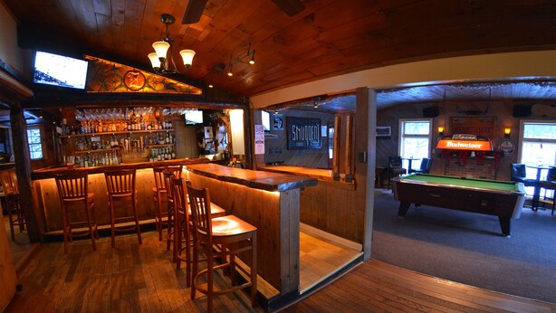 A bar area with wooden furniture, a pool table, and a television mounted on the wall.