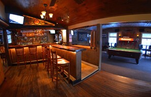 A bar area with wooden furniture, a pool table, and a television mounted on the wall. - Hyde Away Inn (Waitsfield)