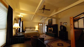 A bedroom with a bed, a desk, a chair, a ceiling fan, a fireplace, and a television.