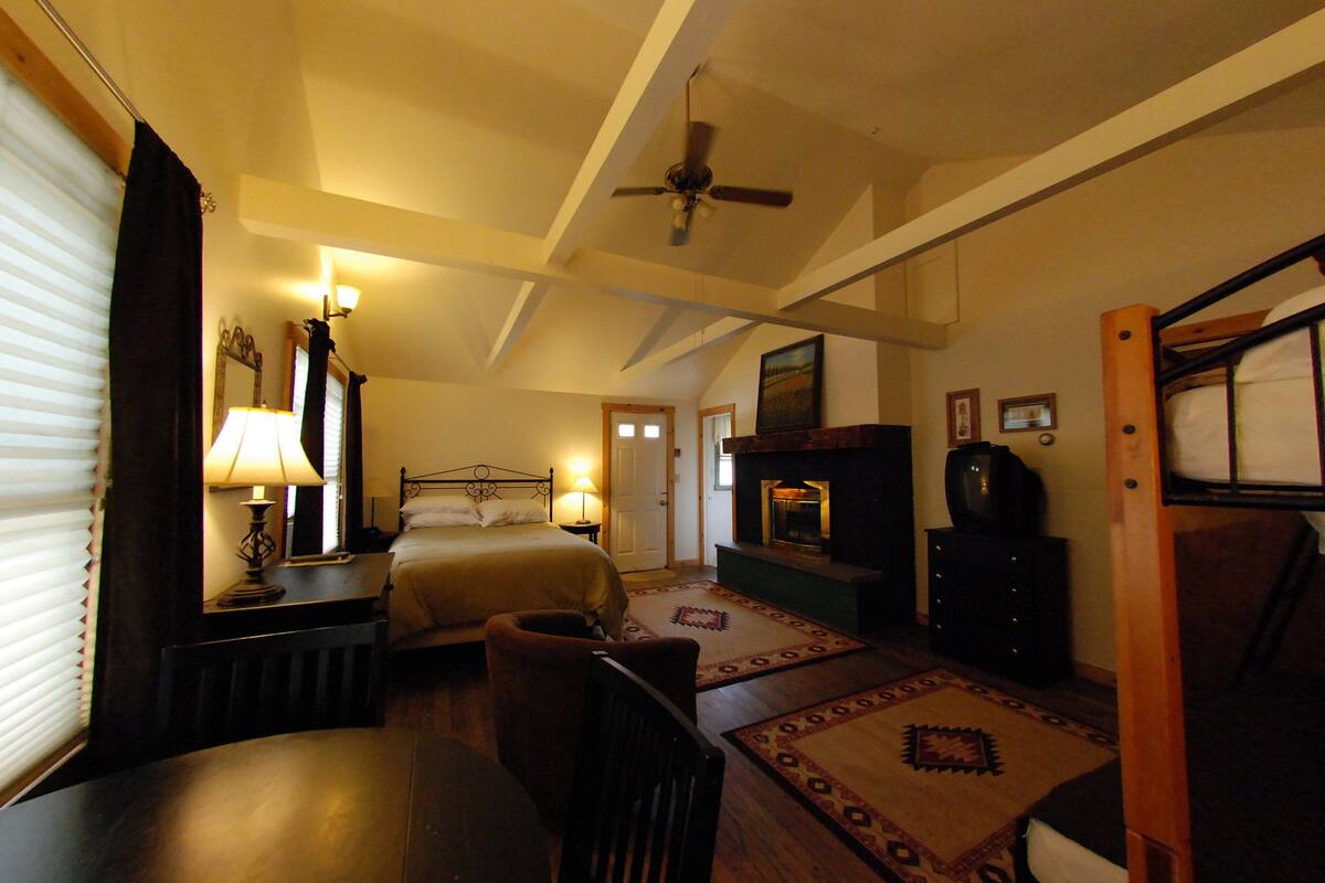 Quarto com cama, escrivaninha, cadeira, ventilador de teto, lareira e televisão.
