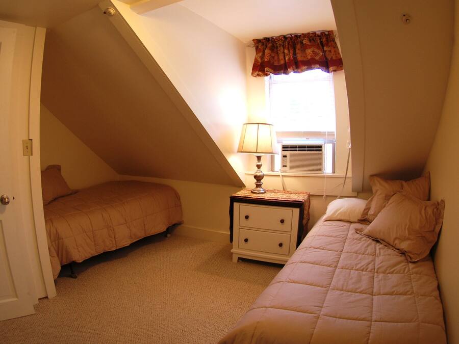 Un dormitorio con dos camas, una mesita de noche con una lámpara y una ventana con cortina.