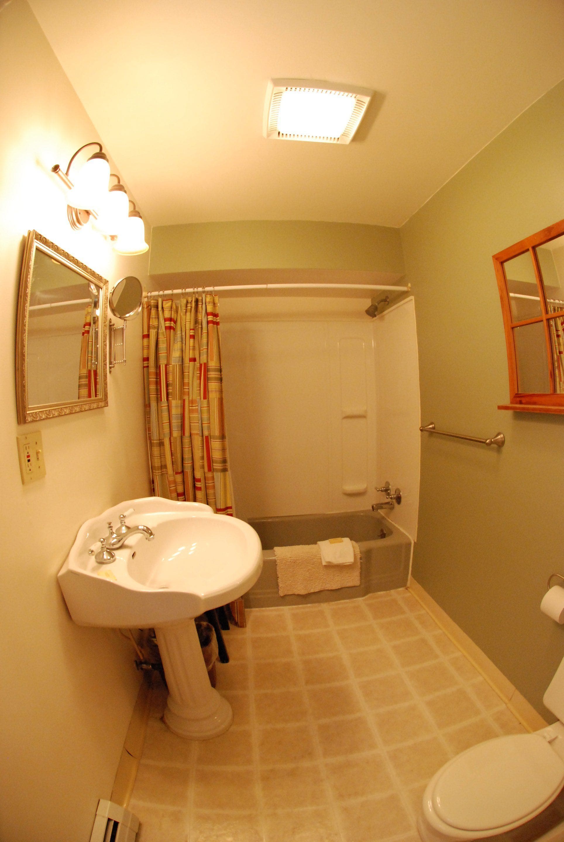 A bathroom with a pedestal sink, a toilet, a shower, and a mirror.