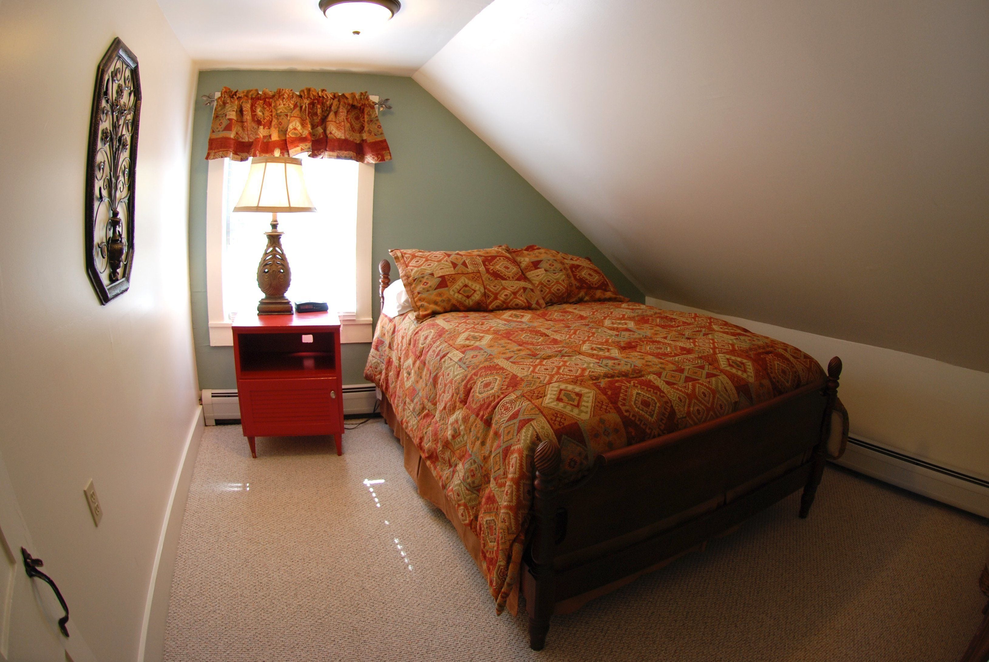 Un dormitorio con cama, mesita de noche, lámpara y ventana con cortinas.
