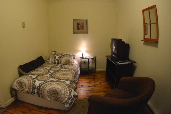 A small, dimly lit room with a bed, a chair, a television, and a small table with a lamp. - Hyde Away Inn (Waitsfield)