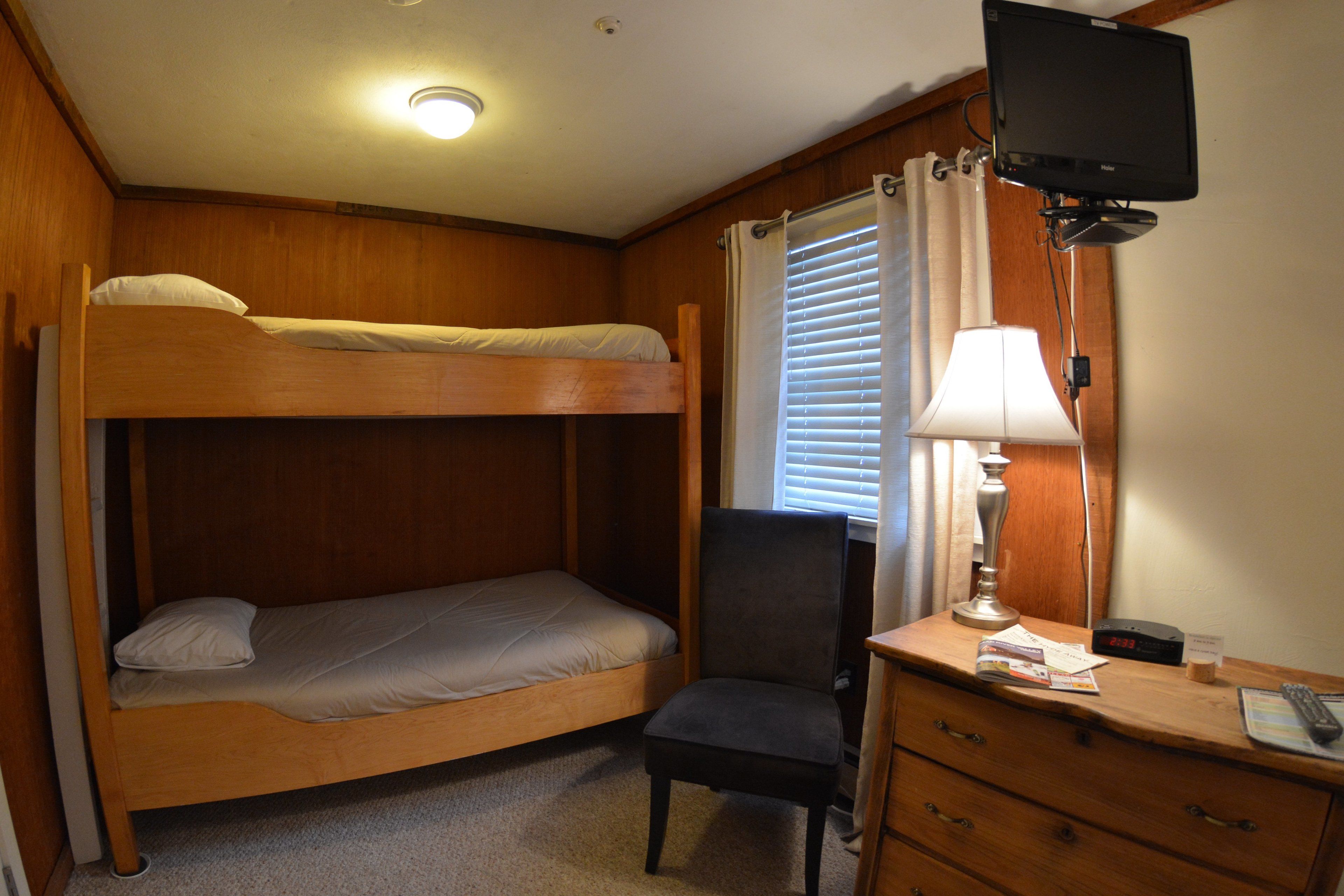 A bunk bed with a desk and chair, a lamp, and a television in a room with wooden walls and a ceiling light.