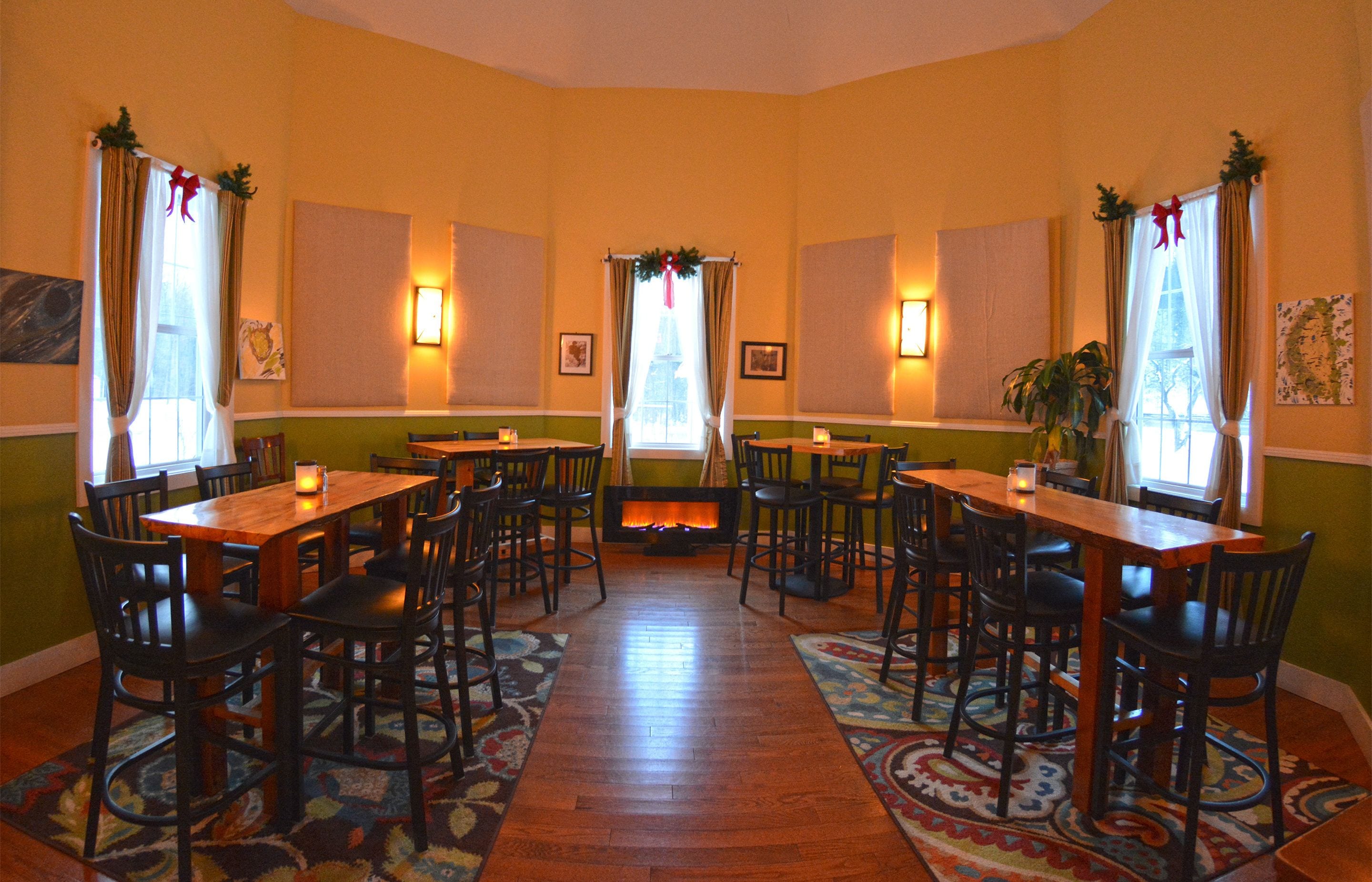 A dining area with wooden tables and chairs, a fireplace, and decorative curtains.