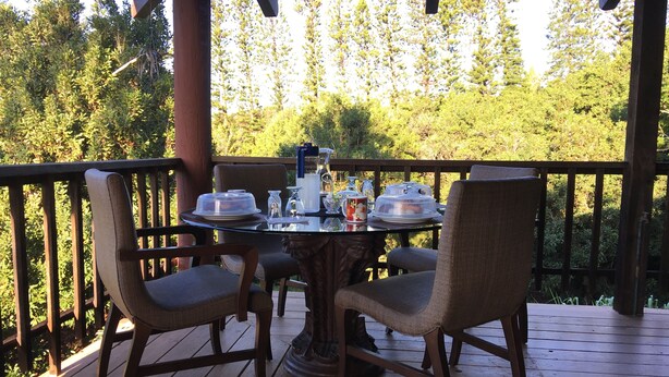 A wooden deck with a round glass table set for four, surrounded by wicker chairs. - Hawaii Island Resort (Naalehu)