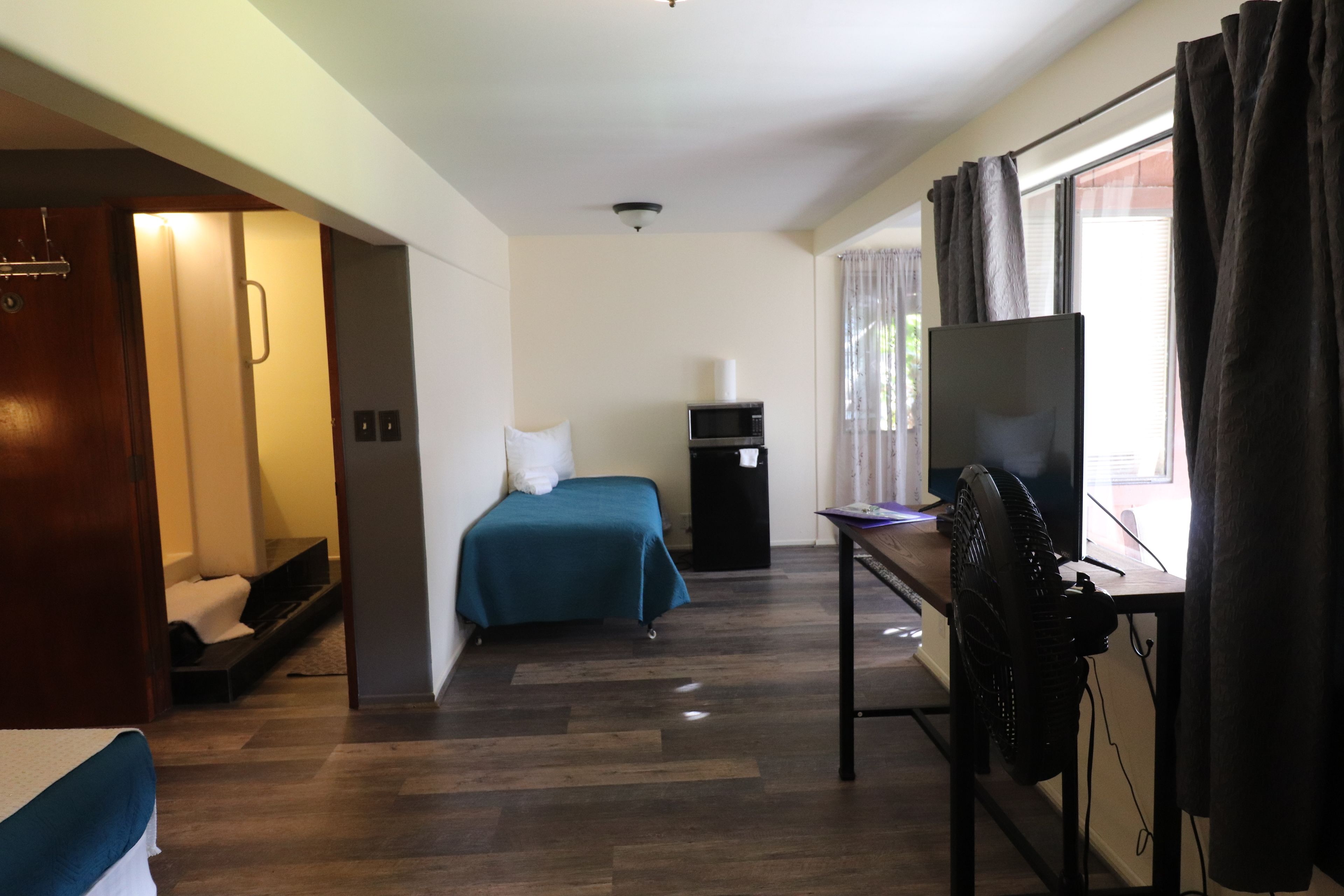 A hotel room with a bed, a desk with a computer, a TV, and a window with curtains.