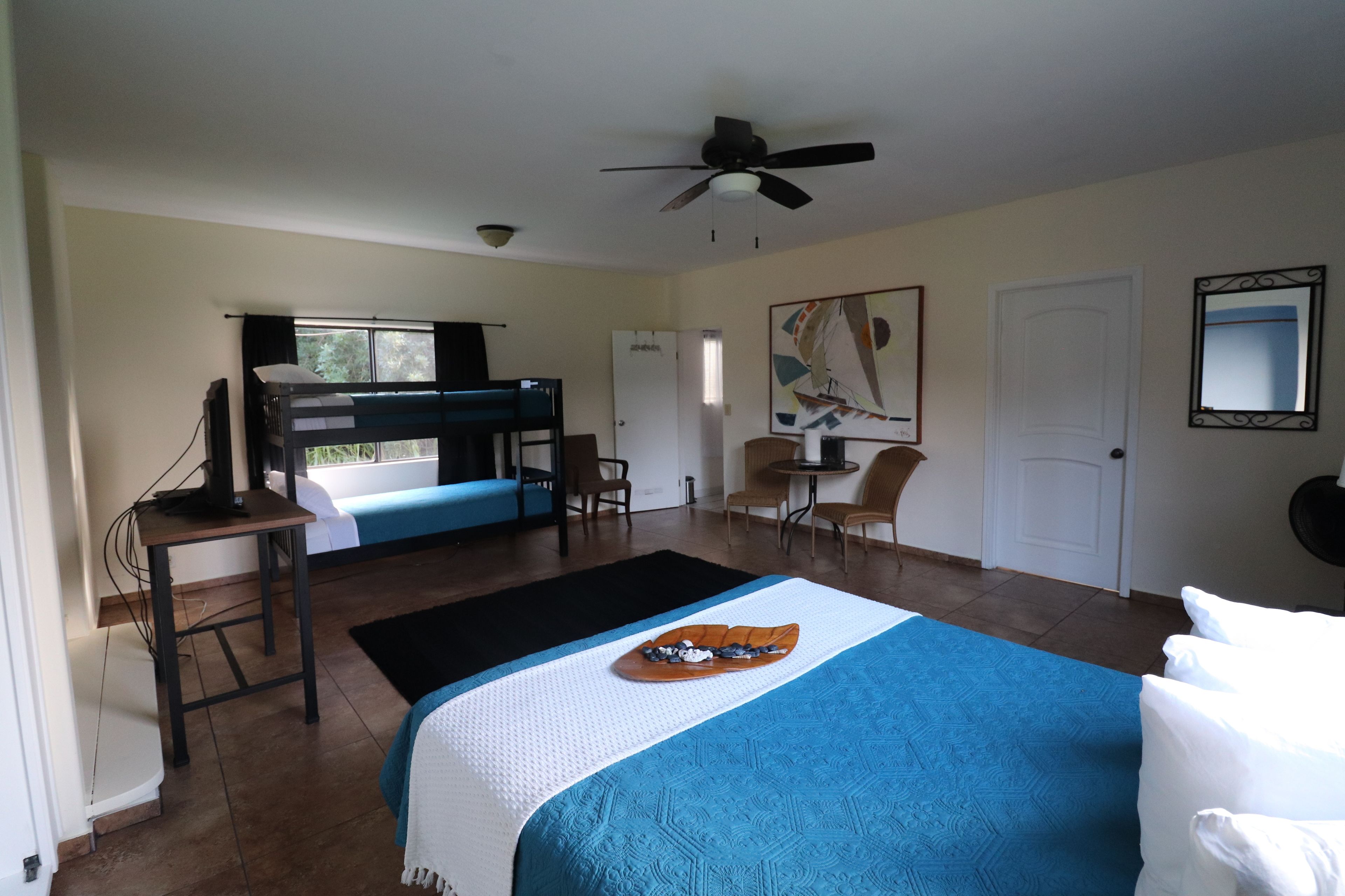 A hotel room with a bunk bed, a desk with a computer, a dining table, and chairs.
