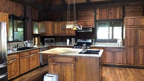 A spacious kitchen with wooden cabinets, granite countertops, a large island, and a hanging light fixture. - Hawaii Island Resort (Naalehu)