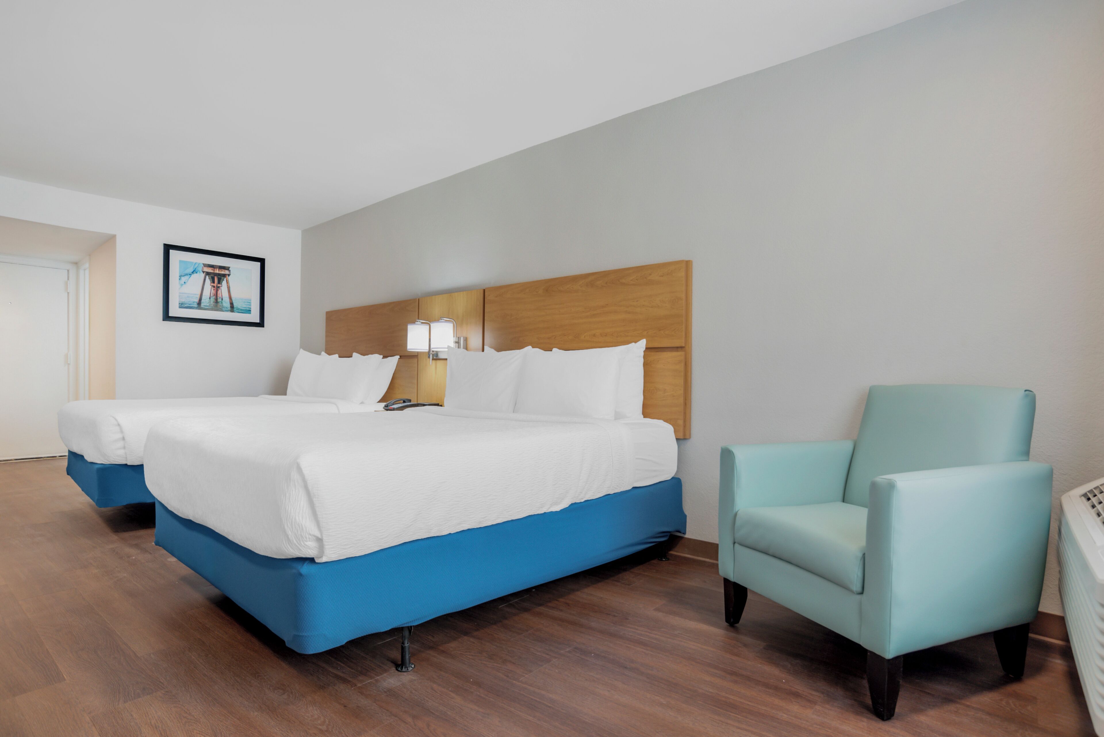 A hotel room with a large bed, a chair, a nightstand, and a framed picture on the wall.