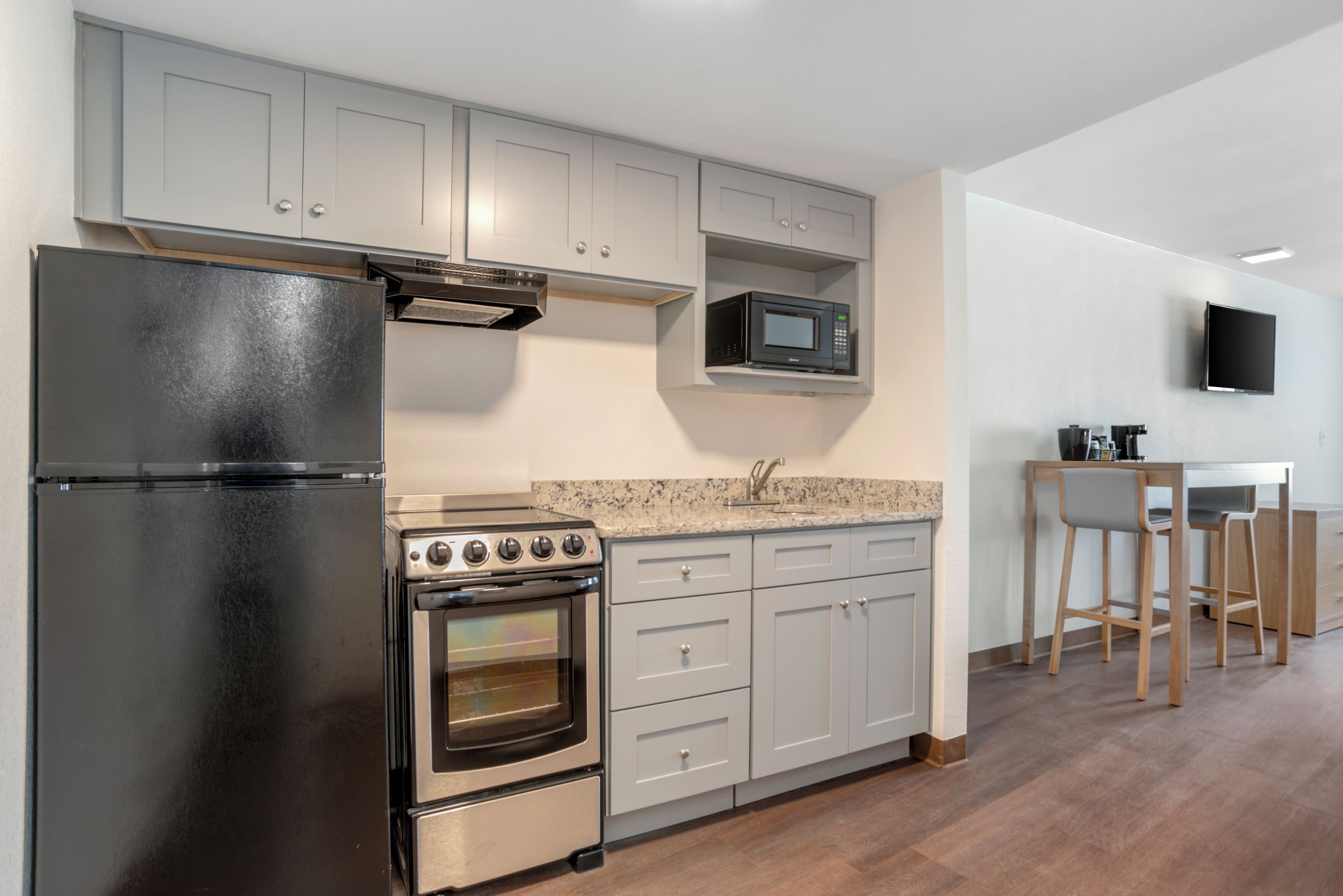 Una cocina con refrigerador, estufa, microondas y televisor montado en la pared.