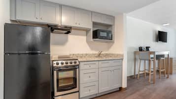 A kitchen with a refrigerator, stove, microwave, and a TV mounted on the wall.