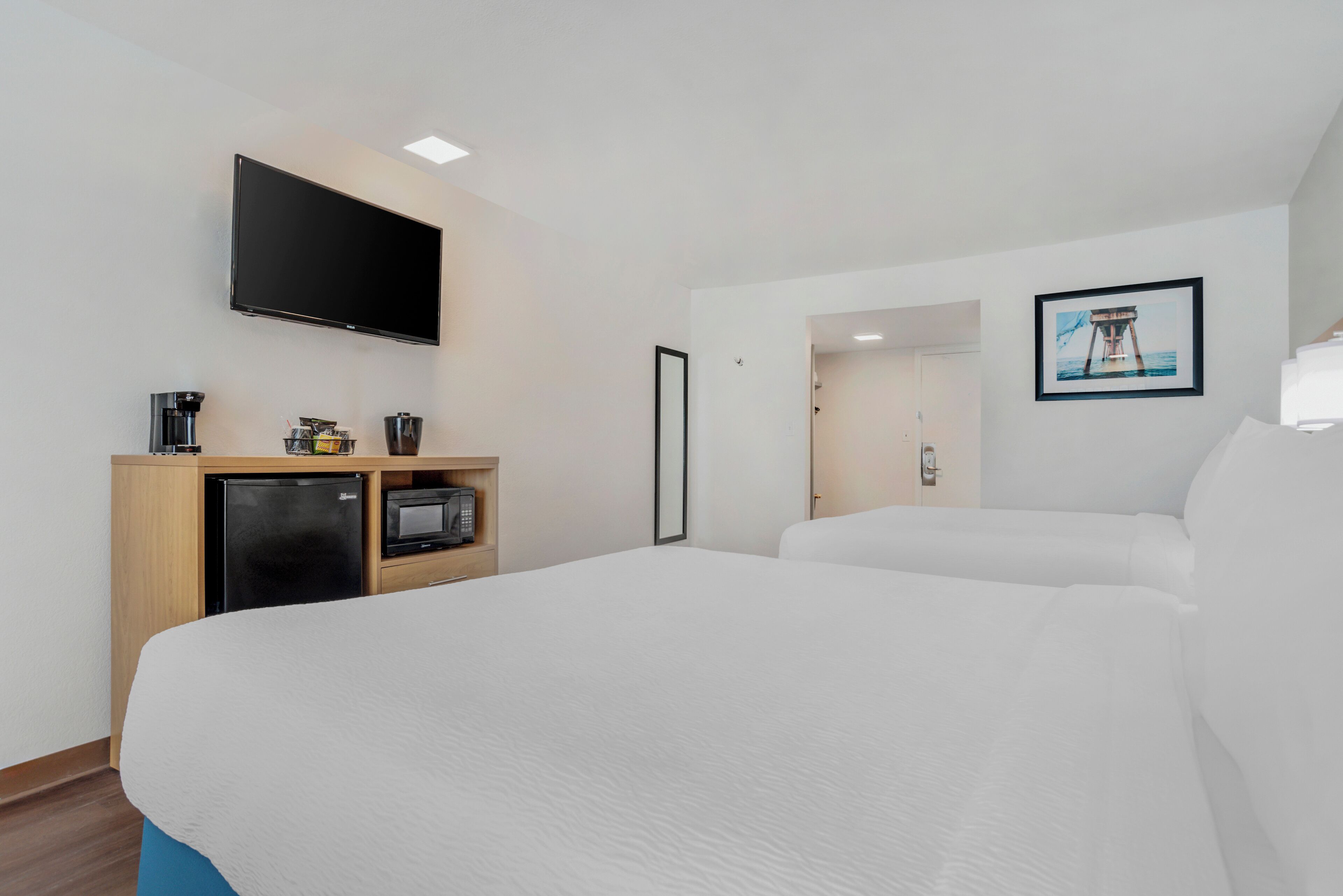 Une chambre d’hôtel dotée d’un grand lit, d’un téléviseur à écran plat fixé au mur, d’une petite kitchenette équipée d’un réfrigérateur, d’un four à micro-ondes et d’une machine à café, ainsi que d’un tableau encadré accroché au mur.