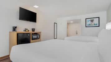 Habitación de hotel con una cama grande, un televisor de pantalla plana montado en la pared, una pequeña kitchenette con refrigerador, microondas y cafetera, y un cuadro enmarcado en la pared.