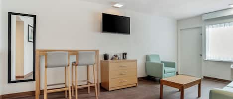 A modern living room with a wooden table, two chairs, a cabinet, a television, and a window.