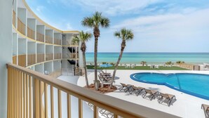 A pool area with lounge chairs, palm trees, and a view of the ocean.