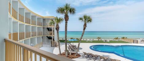 A pool area with lounge chairs, palm trees, and a view of the ocean.
