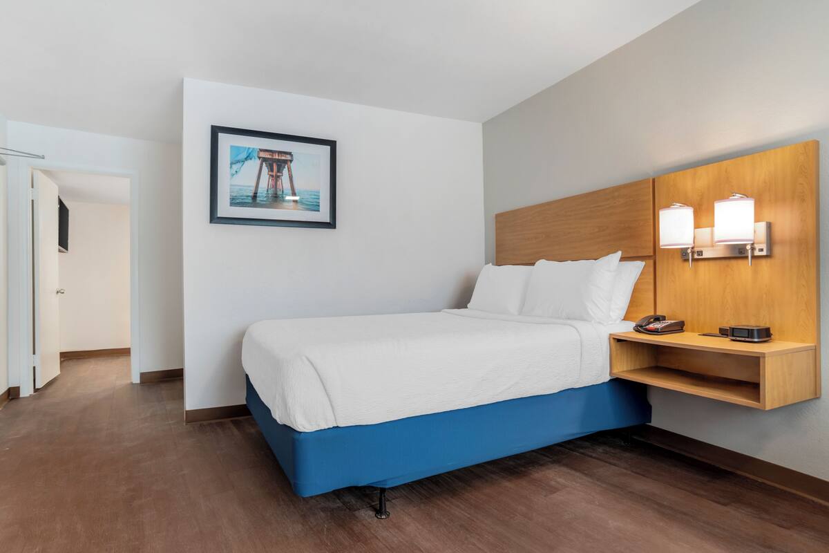 A hotel room with a bed, a wooden headboard, a bedside table with a lamp, and a framed picture on the wall.