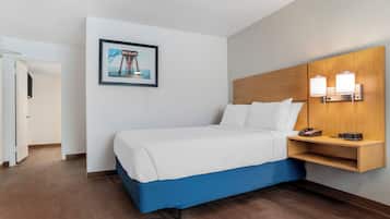 A hotel room with a bed, a wooden headboard, a bedside table with a lamp, and a framed picture on the wall.