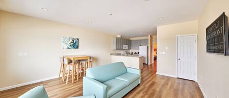 Una sala de estar moderna con un sofá azul claro, una zona de comedor con una mesa de madera y una cocina al fondo.