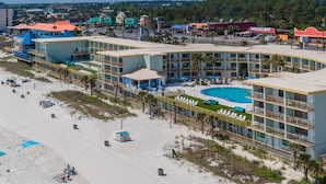 A beachfront hotel with multiple balconies, a swimming pool, and a sandy beach area.