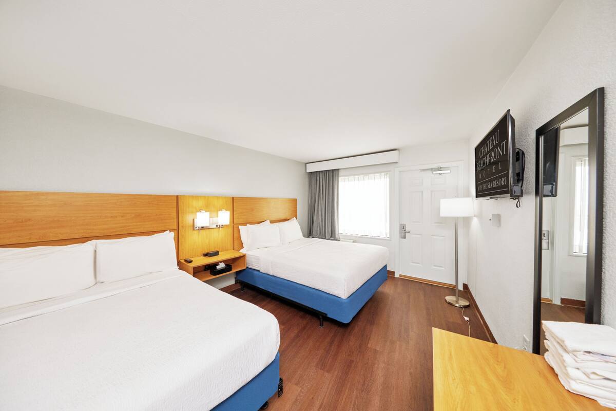 A hotel room with two beds, a wooden headboard, bedside lamps, a flat-screen TV, and a mirror.
