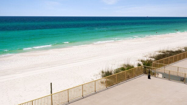 A beach with a clear view of the ocean, a sandy shore, and a yellow railing.