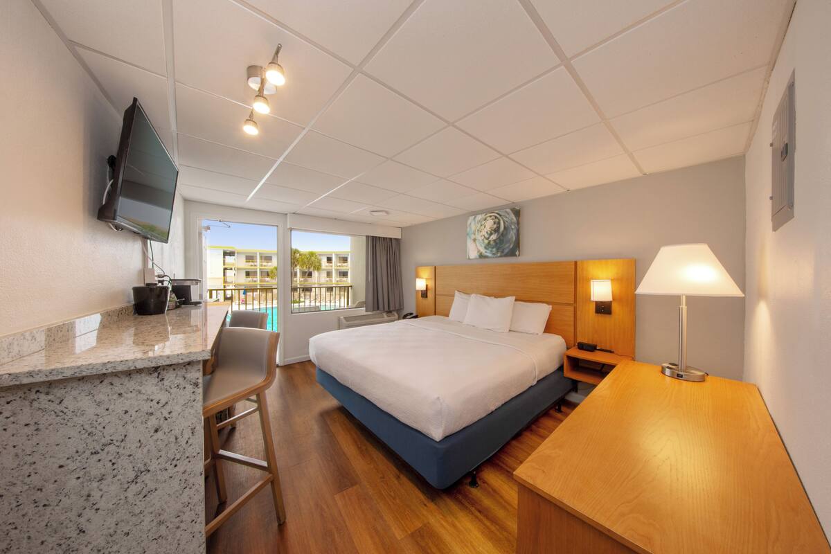 A hotel room with a bed, a desk, a chair, a TV, and a window with a view of buildings.