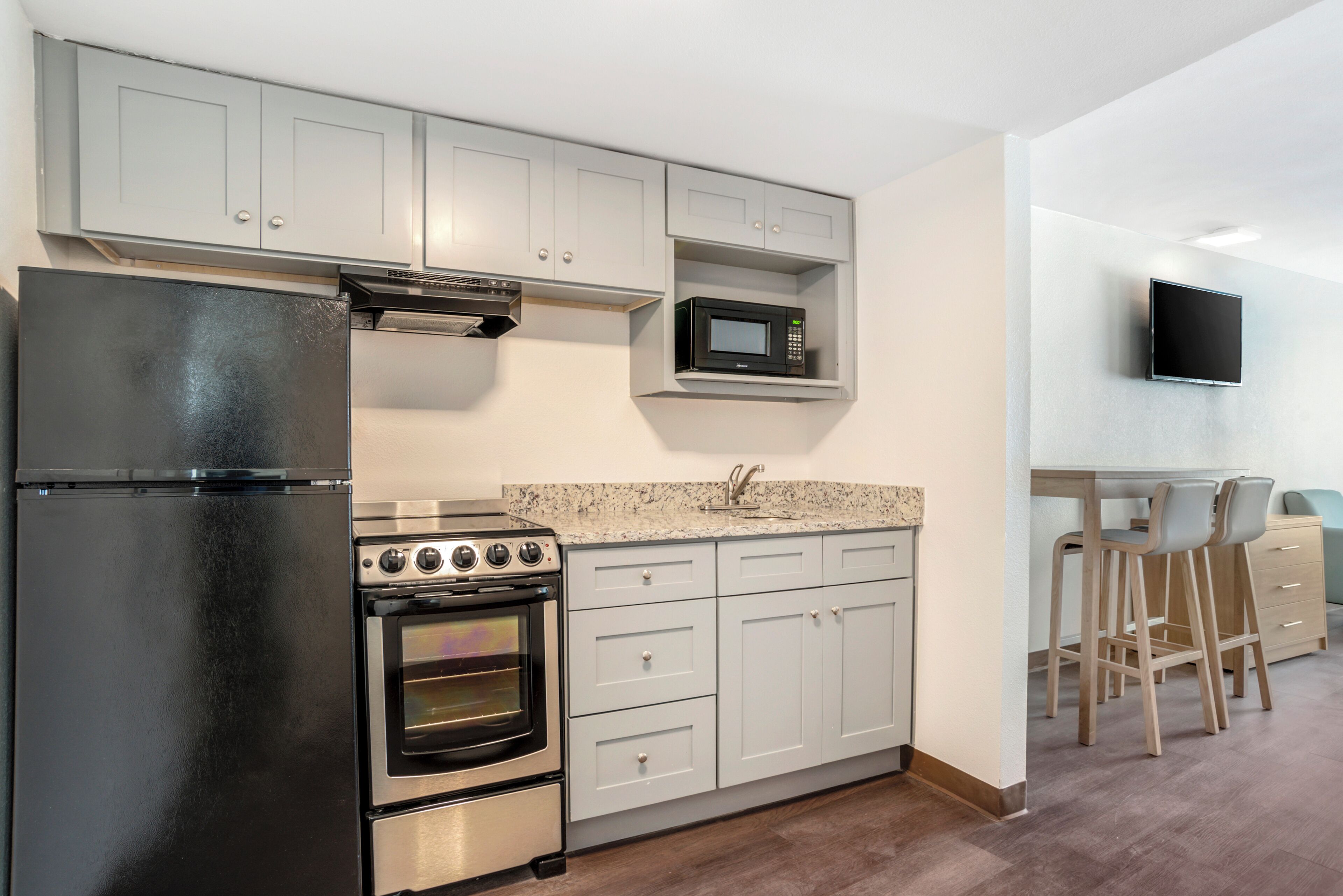 A kitchen with a refrigerator, oven, microwave, and a TV mounted on the wall.